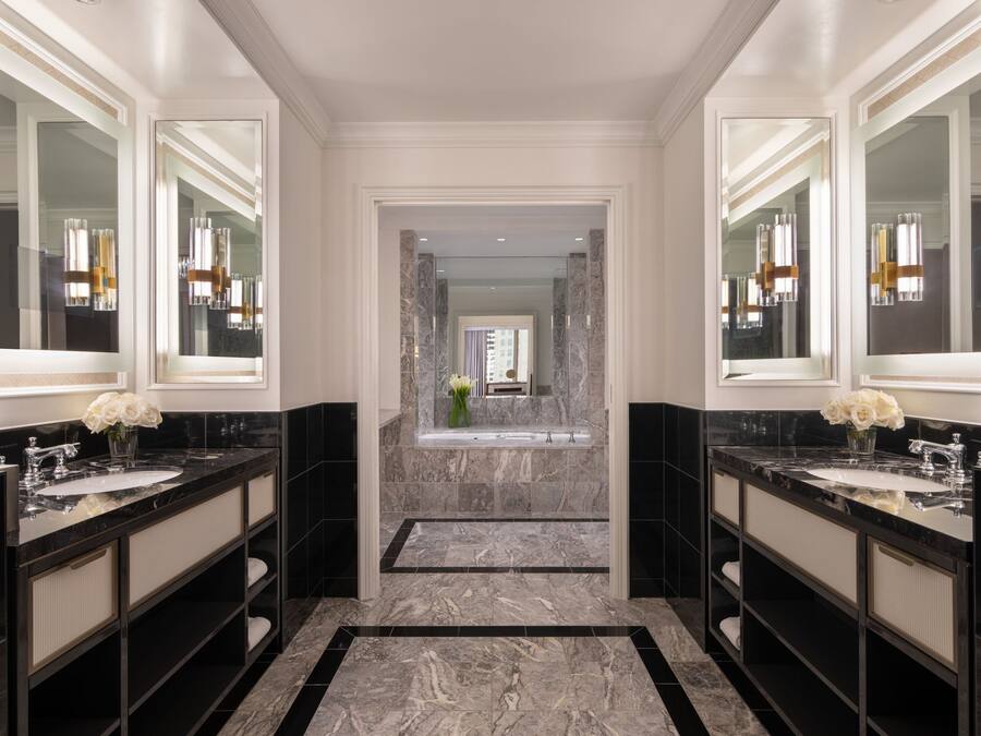 A luxurious bathroom with two large marble sinks, a central bathtub, and a mirror above each sink.