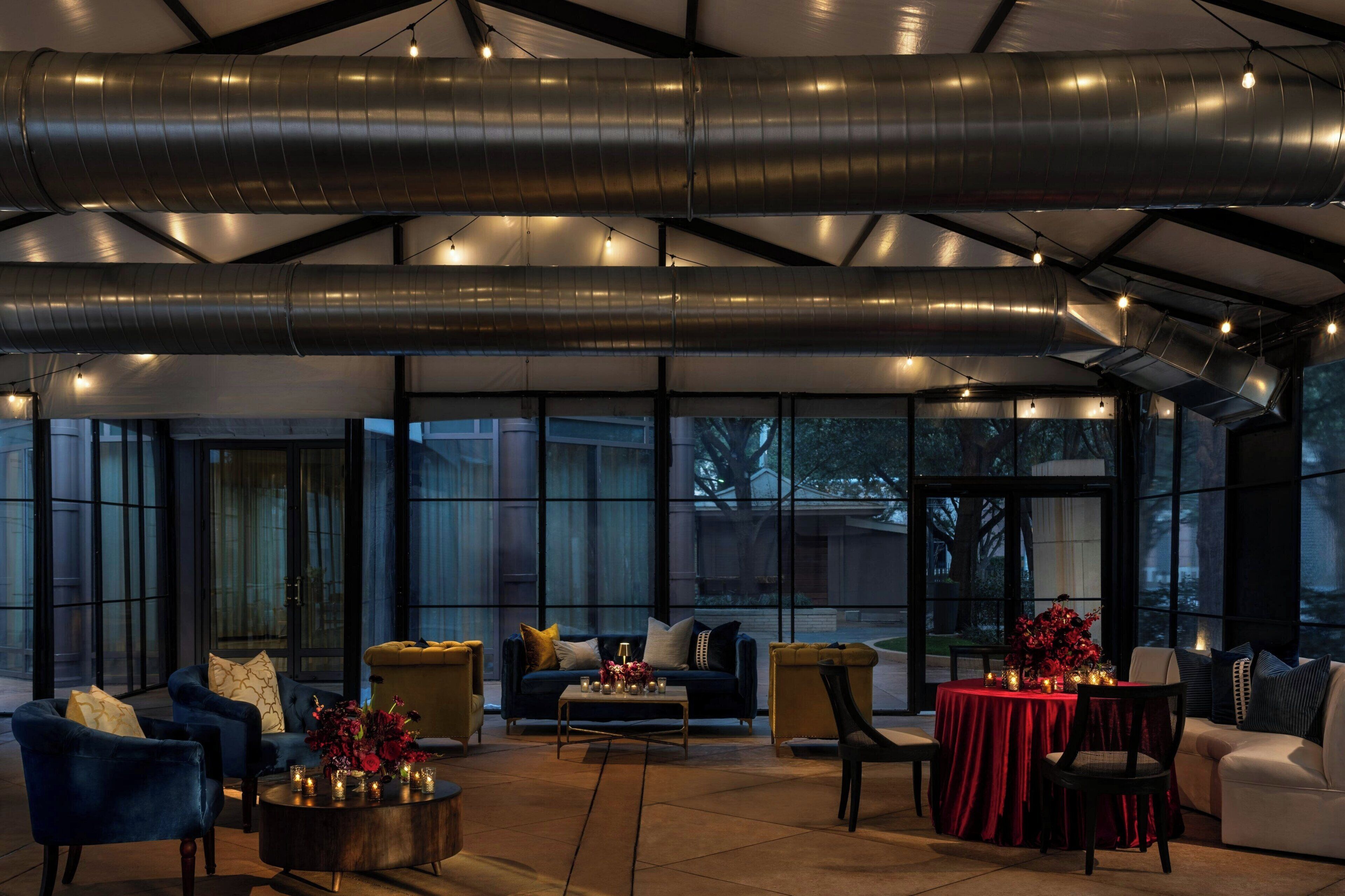 Un espacio interior amplio con arreglos de asientos, una mesa con mantel rojo y ventanas grandes que ofrecen vistas al exterior.