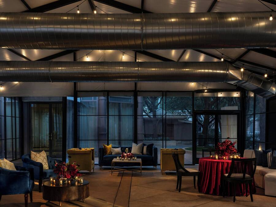 Un espacio interior amplio con arreglos de asientos, una mesa con mantel rojo y ventanas grandes que ofrecen vistas al exterior.