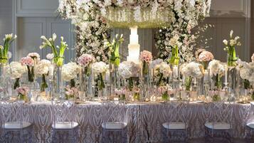 A long table with clear chairs, adorned with floral arrangements and candles, set against a wall with a decorative arch.