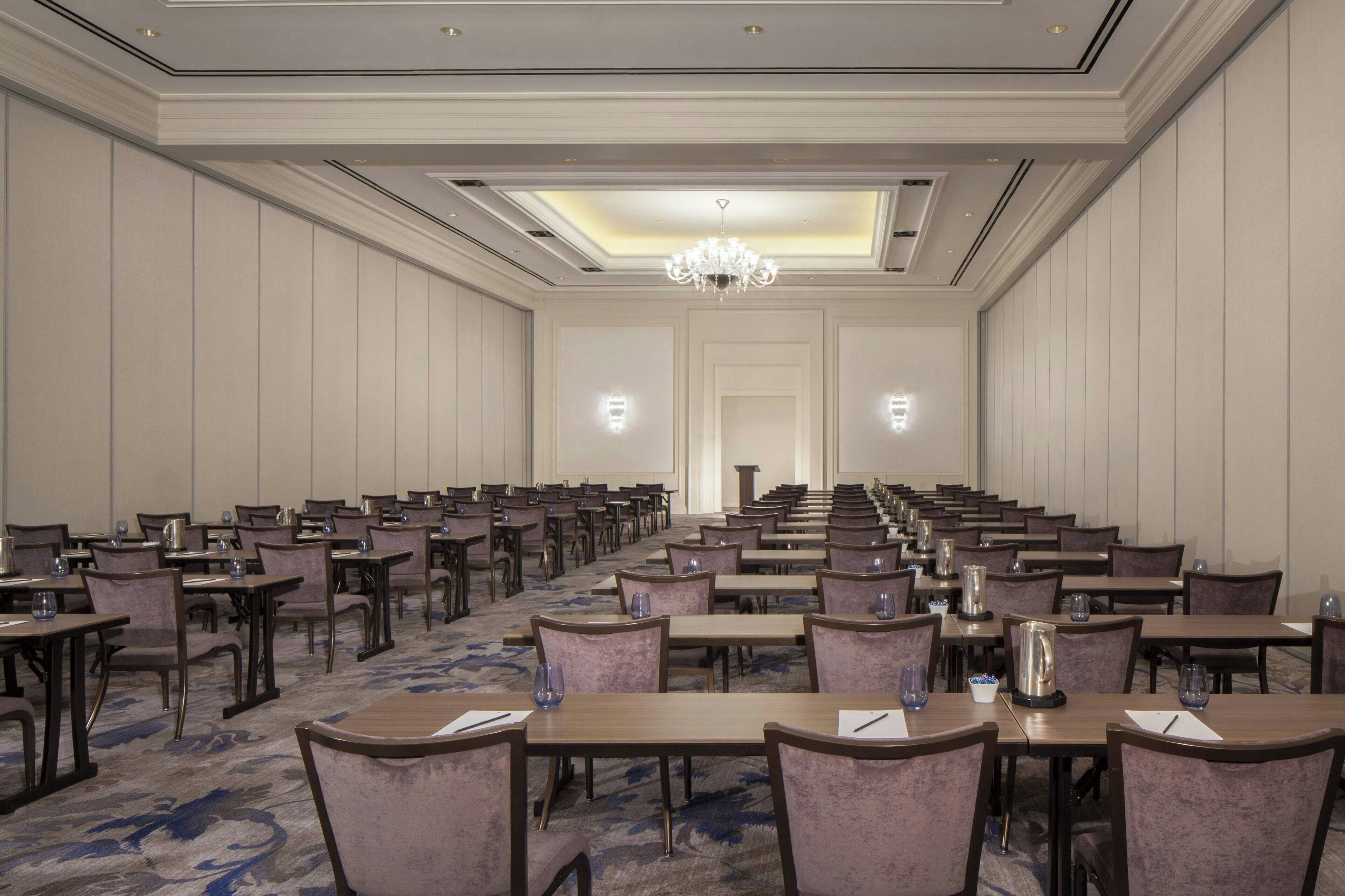 A large conference room with rows of tables and chairs, a chandelier, and a carpeted floor.
