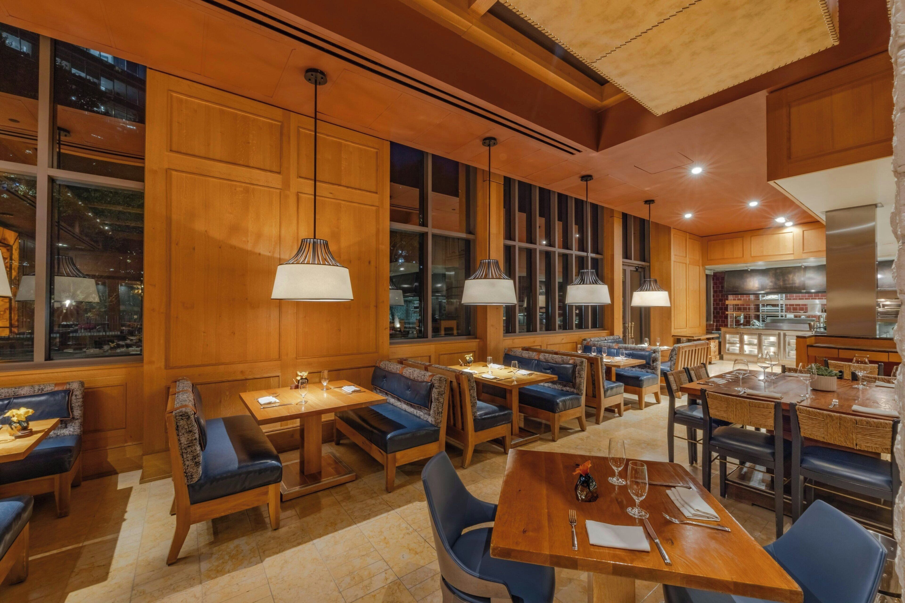 A restaurant with wooden furniture, large windows, and pendant lighting.