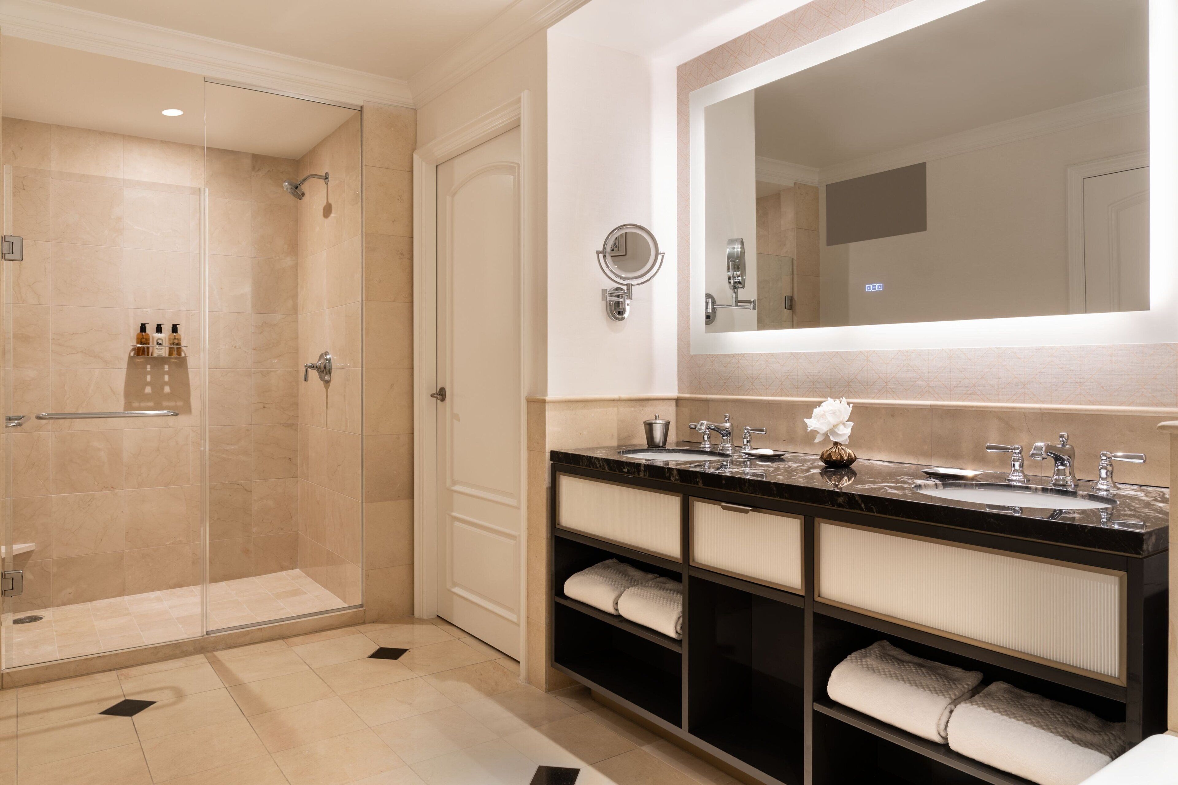 A modern bathroom with a glass-enclosed shower, a large mirror, and a vanity with two sinks.