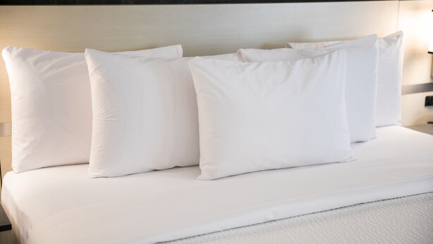 A neatly made bed with white bedding and pillows. - Nova Inn Yellowknife (Yellowknife)