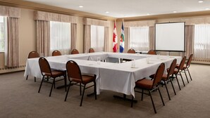 A conference room with a long table, chairs, flags, and a projector screen. - Nova Inn Yellowknife (Yellowknife)