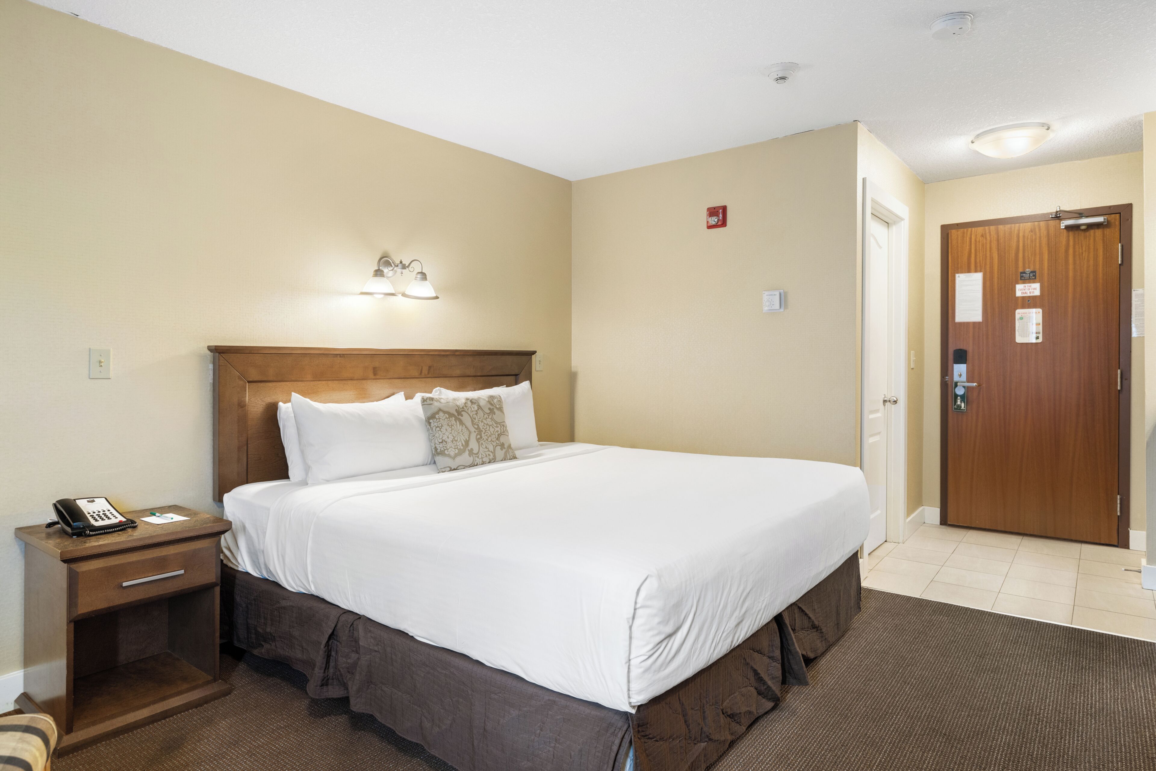 A hotel room with a single bed, a nightstand, a phone, and a door with a sign.