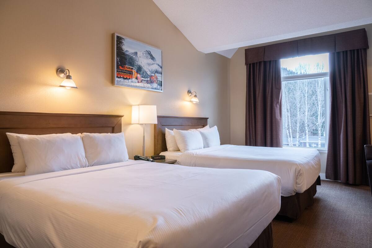 Una habitación de hotel con dos camas, un cuadro en la pared y una ventana con cortinas.