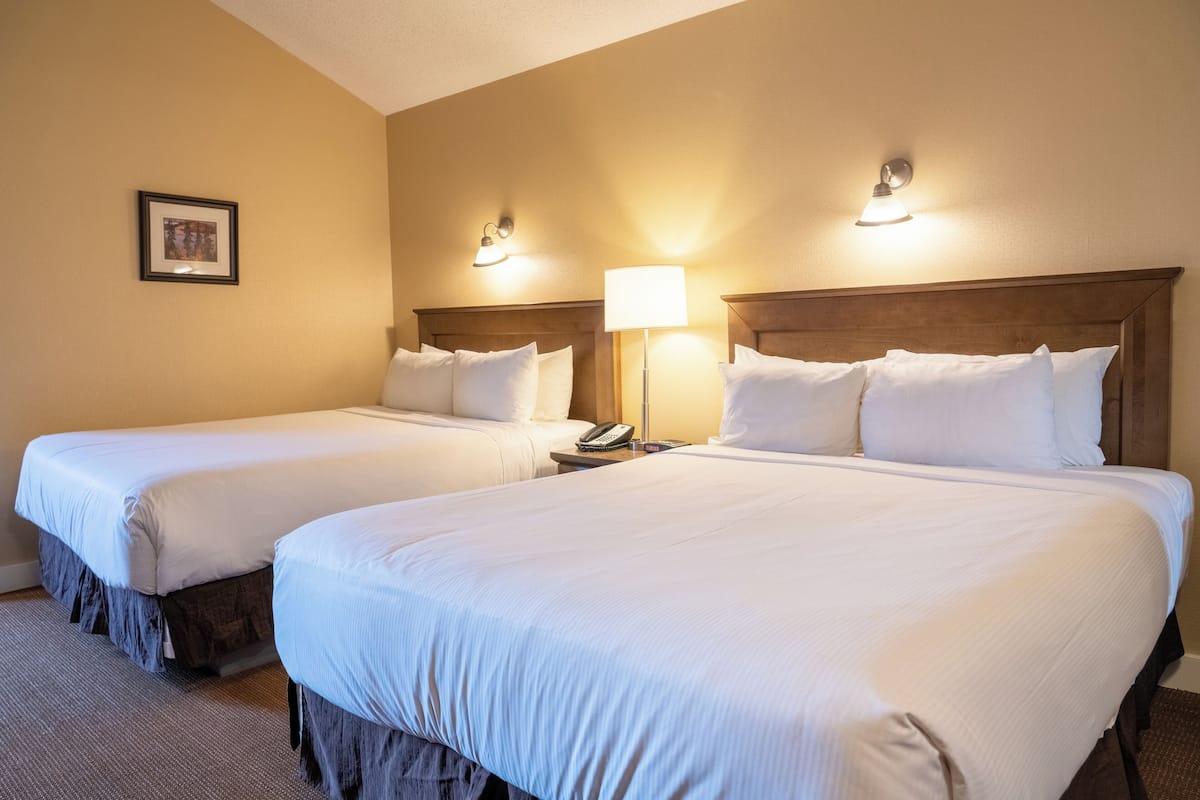 Habitación de hotel con dos camas, una mesita de noche con lámpara y un cuadro enmarcado en la pared.