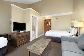 A hotel room with a bed, a sofa, a TV, a dresser, and a small table. - Irwin's Mountain Inn (Banff)
