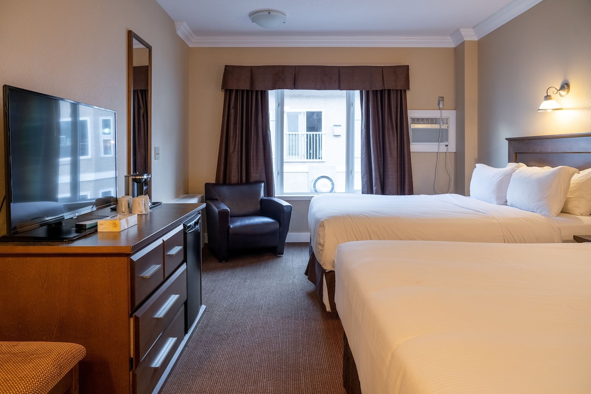 Habitación de hotel con una cama, un escritorio con televisor de pantalla plana, una silla y una ventana con cortinas.