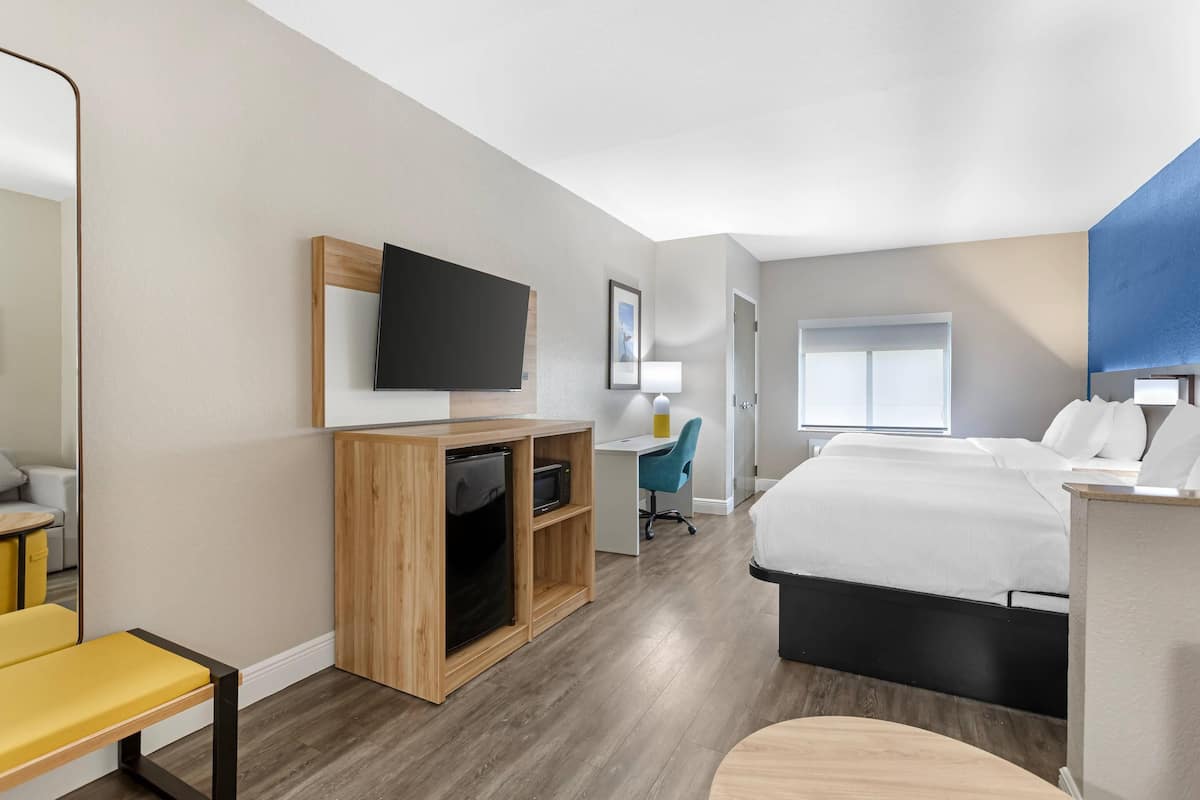 Habitación de hotel con cama, escritorio, televisor, silla y un pequeño rincón de descanso.