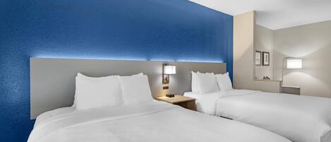 A hotel room with two beds, a nightstand with a lamp, and a wall-mounted mirror.