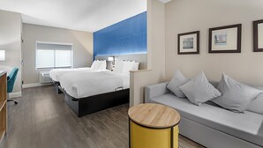 A modern hotel room with a bed, a sofa, a small table, and a window. - Comfort Suites West Jacksonville (Jacksonville)