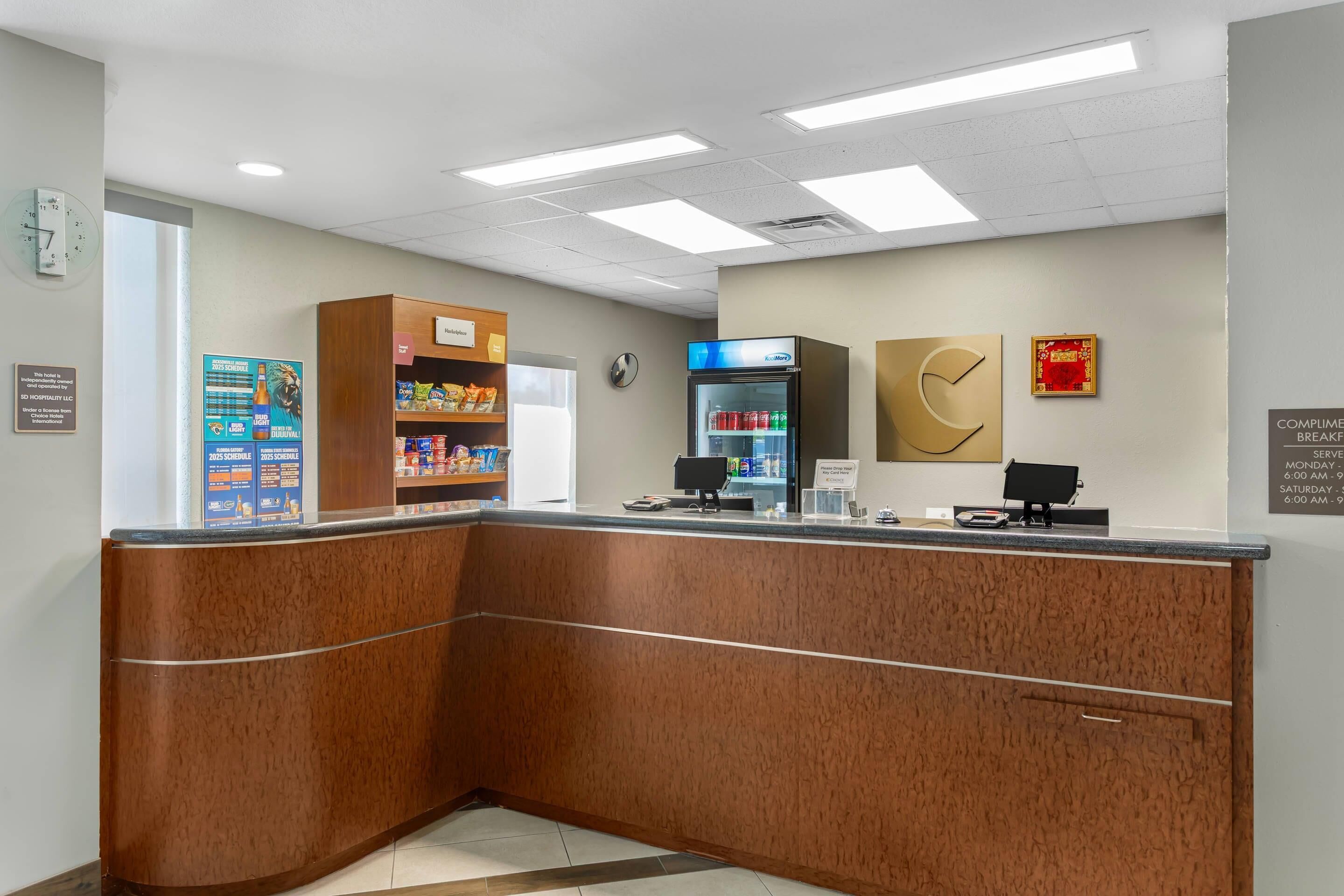 A reception area with a wooden counter, a refrigerator, a clock, and a wall with a framed picture and a sign.