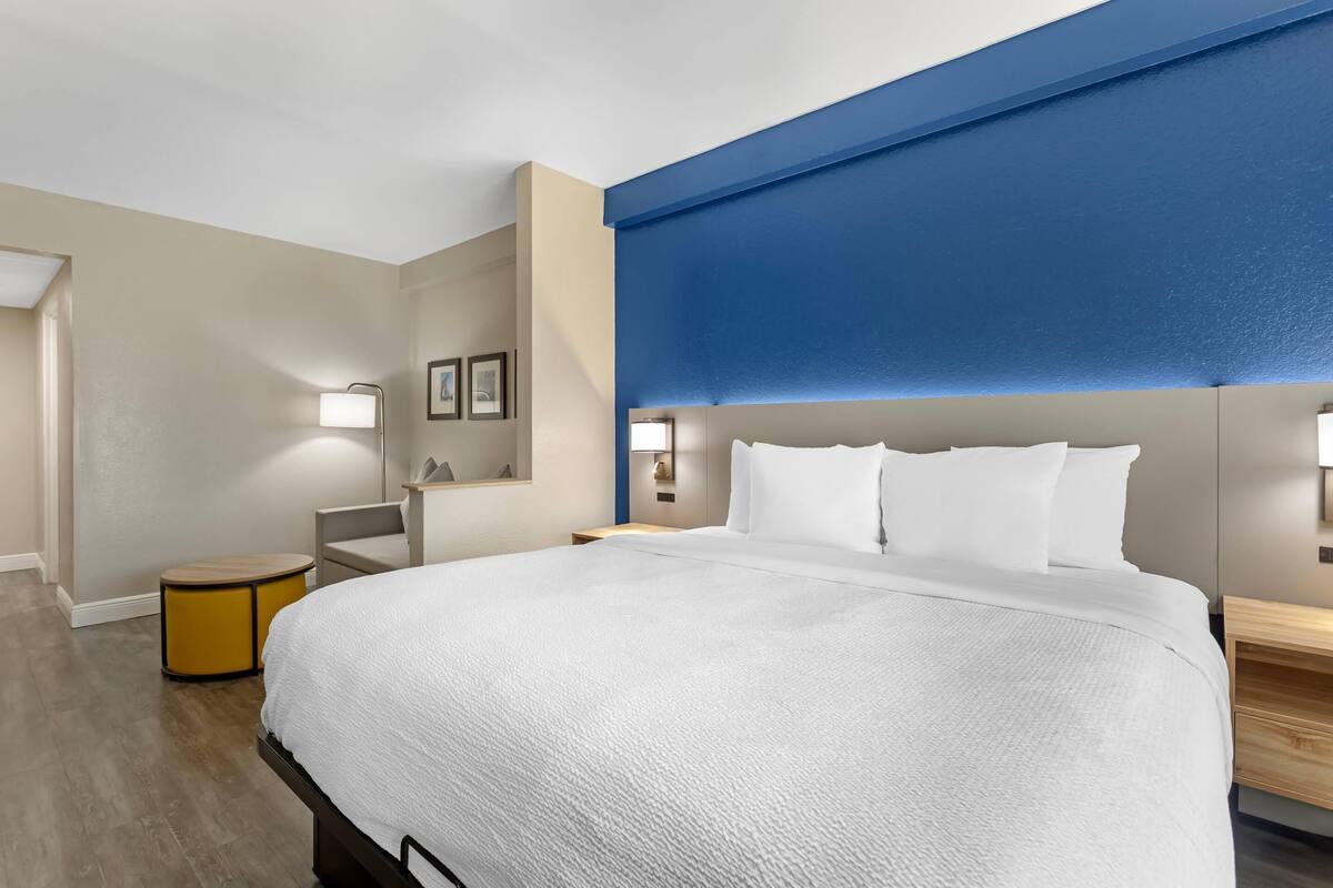 Habitación de hotel con una cama grande, mesitas de noche, una lámpara y un estante en la pared.