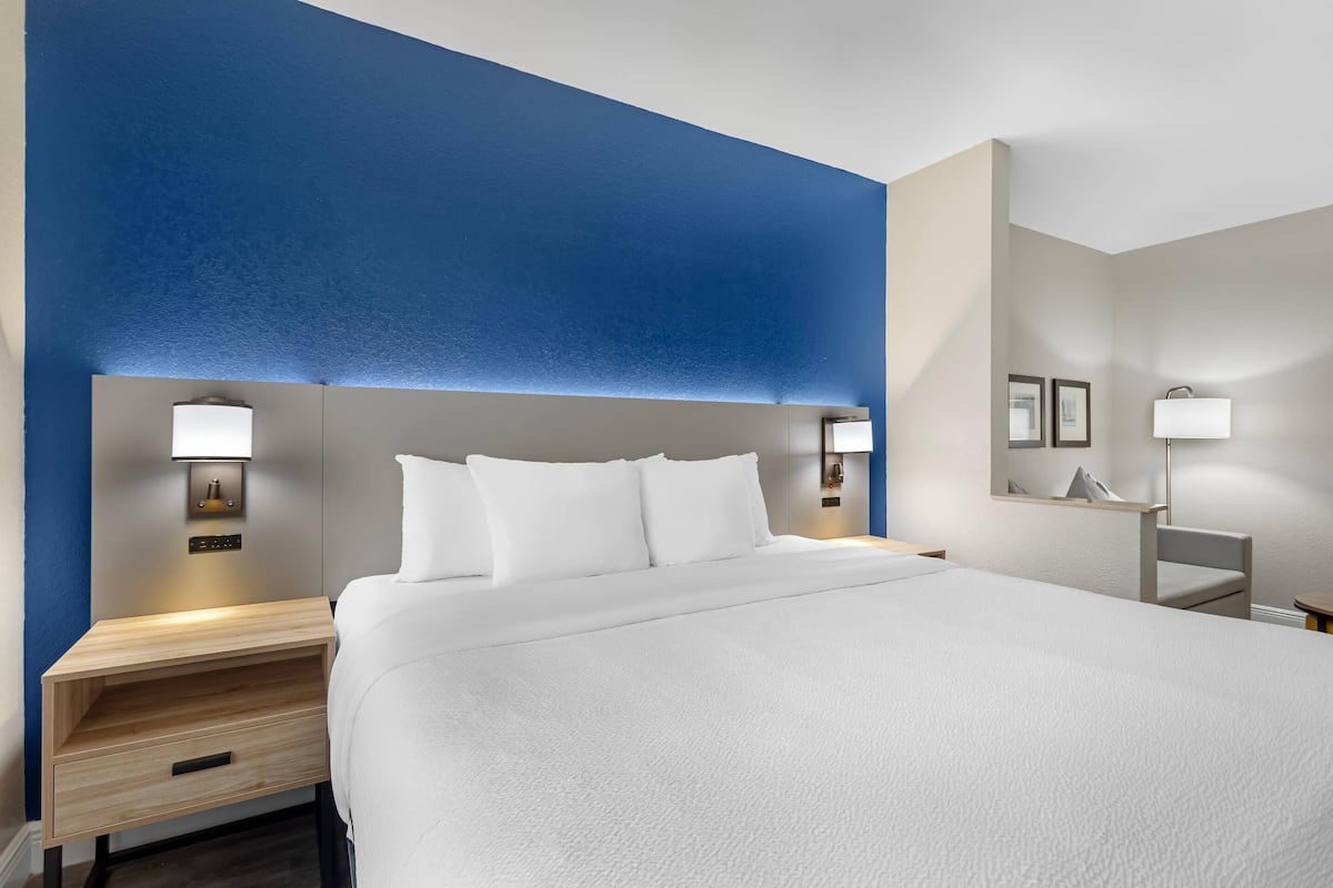 Una habitación de hotel con una cama grande, mesitas de noche con lámparas, un aparador con cajón y un espejo colgado en la pared.