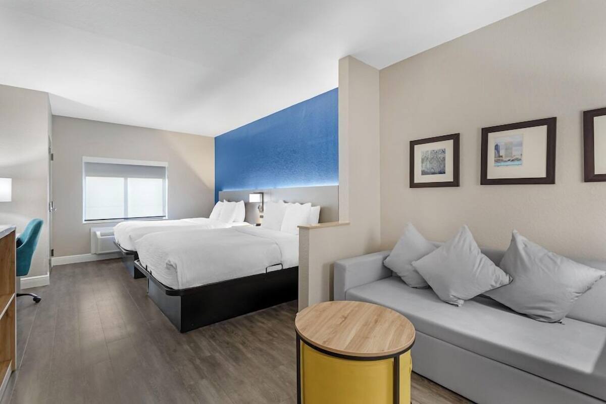 Una habitación de hotel moderna con una cama, un sofá, una mesita y un ventanal.