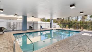An indoor swimming pool with a tiled floor, a metal pool ladder, and a covered area with a white ceiling and ceiling lights.