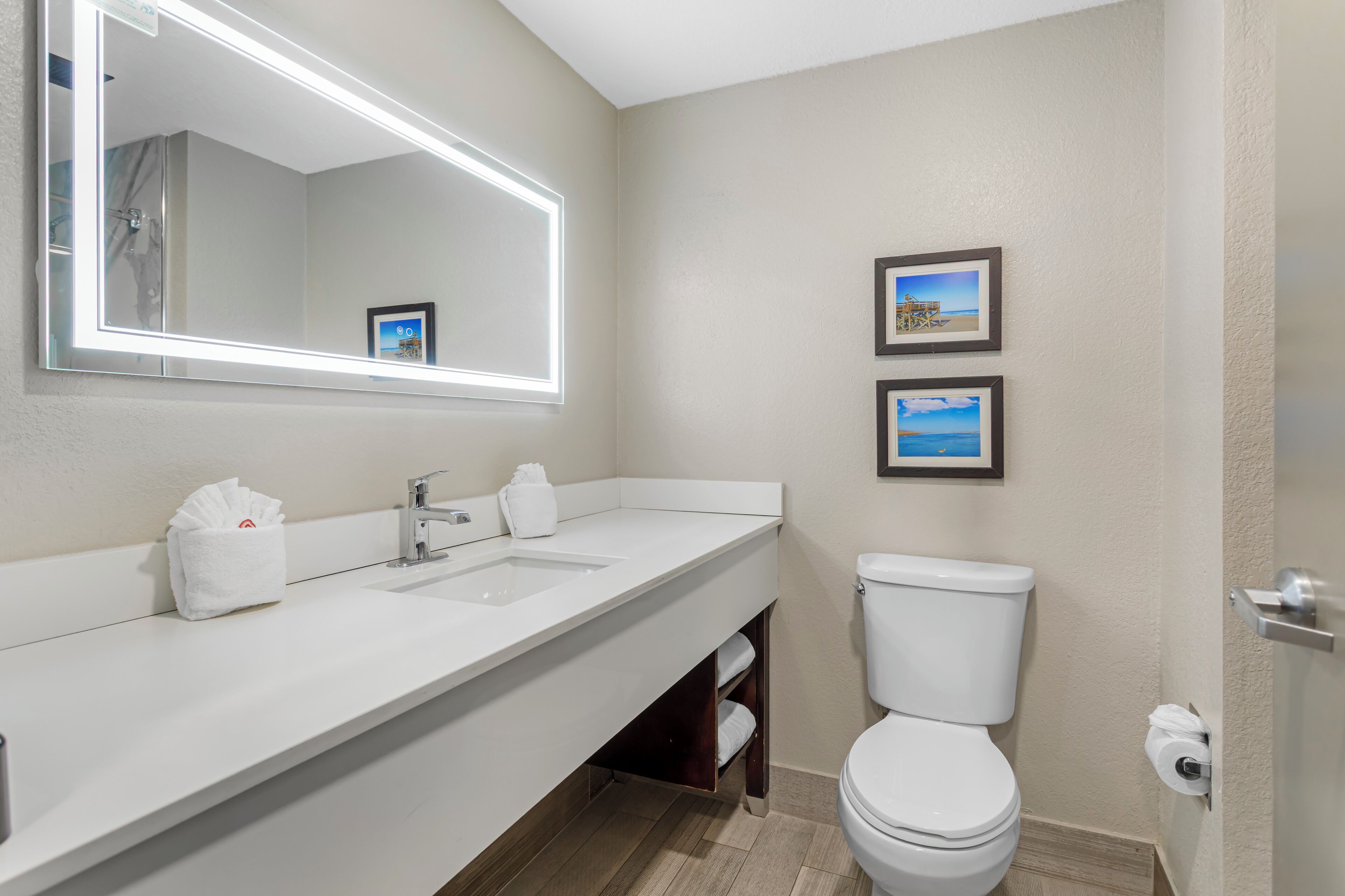 A bathroom with a white sink, mirror, and toilet. There are two framed pictures on the wall.
