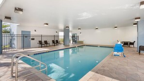 An indoor swimming pool with a tiled floor, a metal pool ladder, and a blue lounge chair. - Comfort Suites West Jacksonville (Jacksonville)