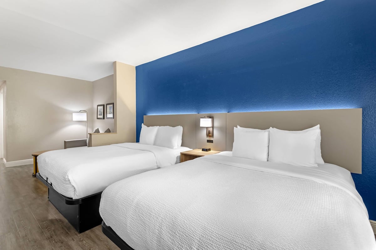 Una habitación de hotel con dos camas, una pared decorada en azul y piso de madera.