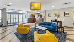A hotel lobby with a reception desk, seating area with yellow and blue sofas, and a large window. - Comfort Suites West Jacksonville (Jacksonville)