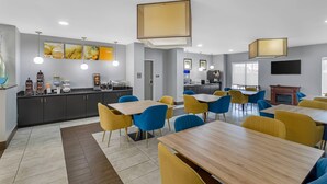 A modern dining area with tables and chairs, a kitchen area, and a flat-screen TV mounted on the wall. - Comfort Suites West Jacksonville (Jacksonville)