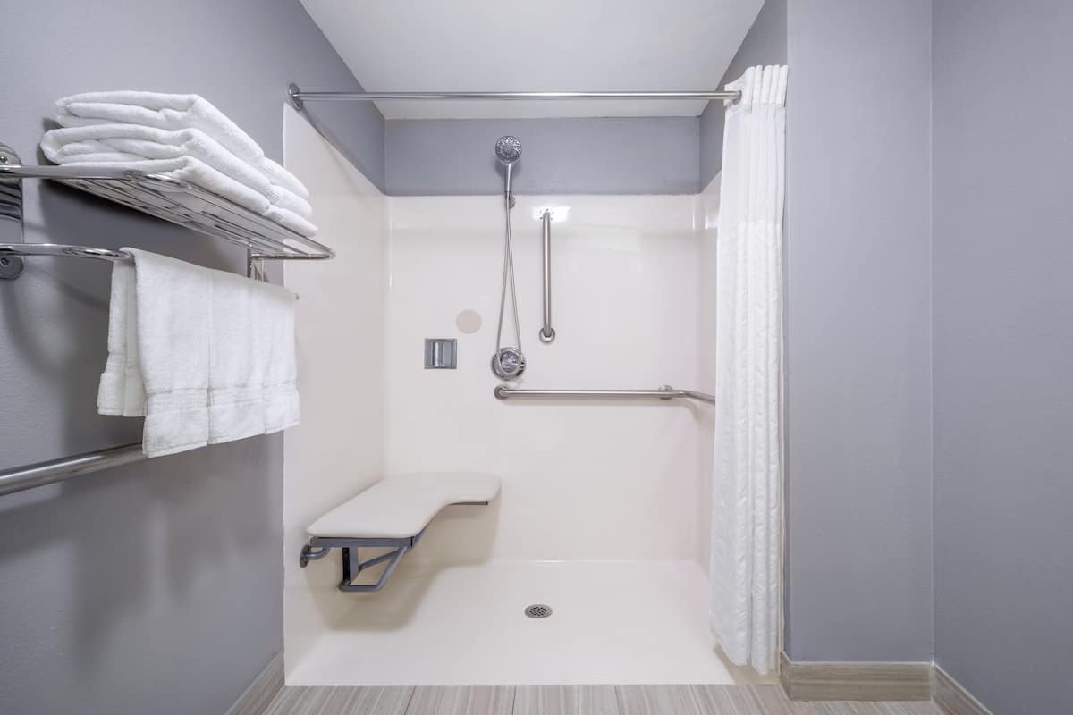 Un baño moderno con ducha a nivel, barras de apoyo, un asiento y un perchero para toallas.