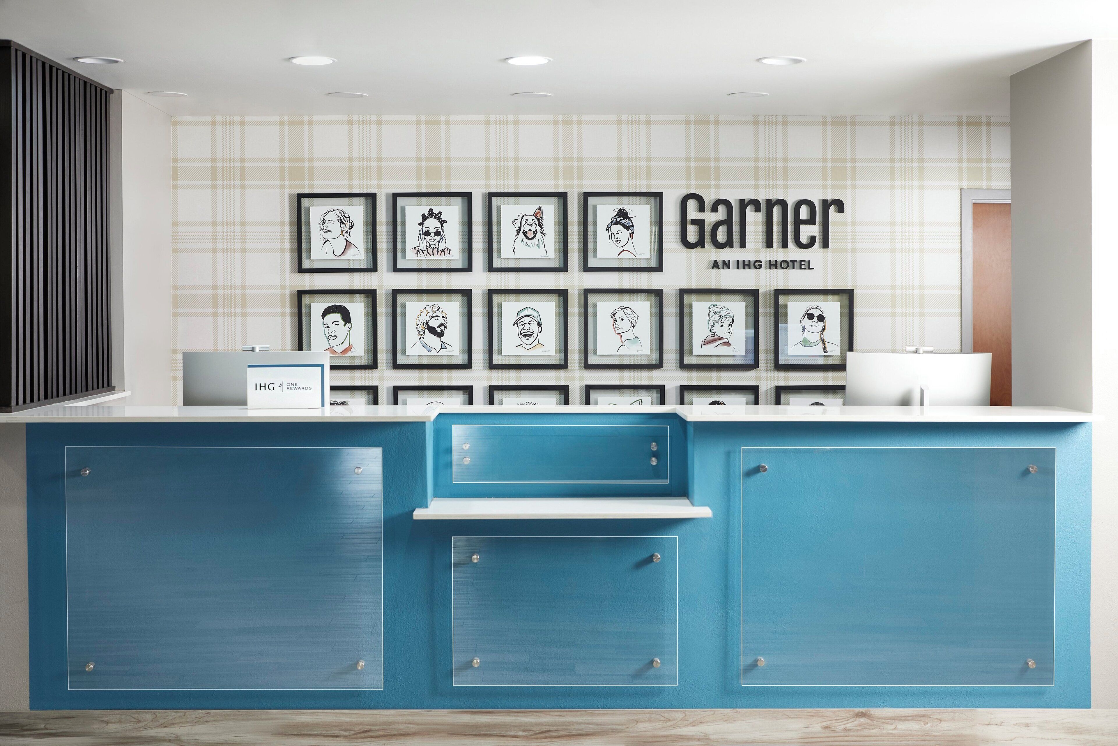 A hotel reception area with a blue counter, framed artwork on the wall, and a sign reading "Garner An IHG Hotel".