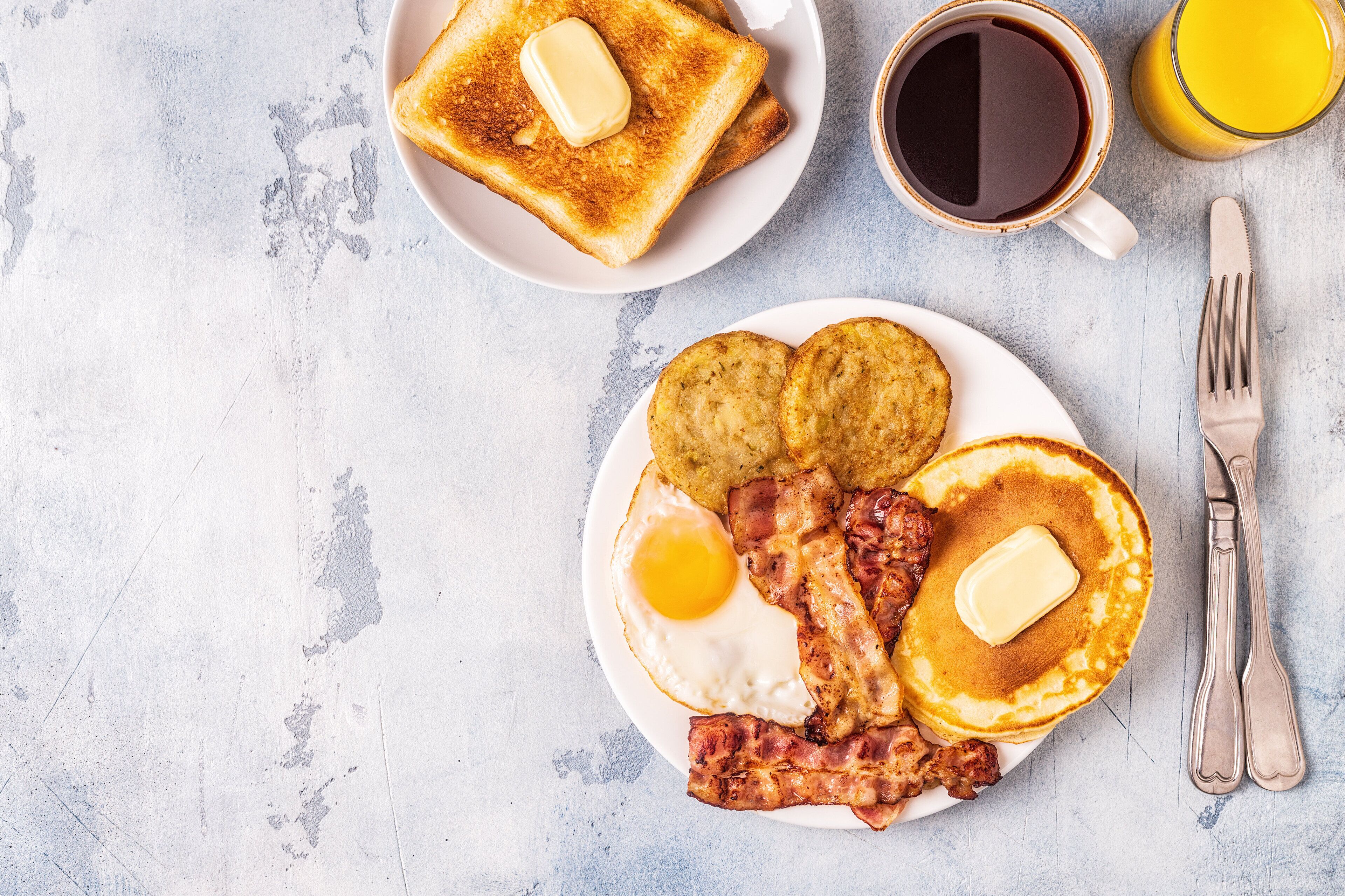 A breakfast plate with toast, eggs, bacon, and pancakes, accompanied by a cup of coffee and a glass of orange juice.