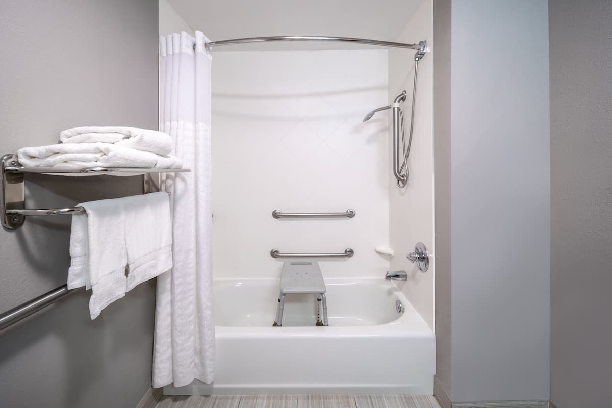 Un baño moderno con ducha a nivel, barras de apoyo y un perchero para toallas.