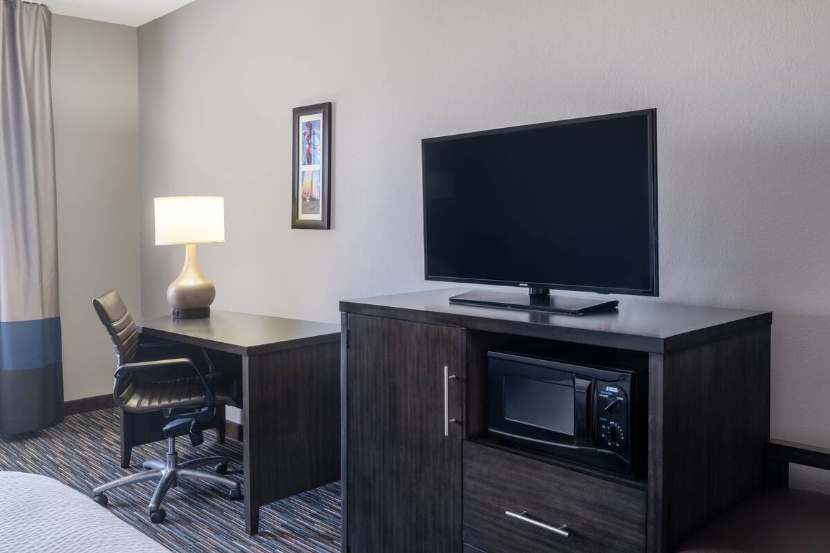 Habitación de hotel con escritorio, silla, televisión, lámpara y microondas.