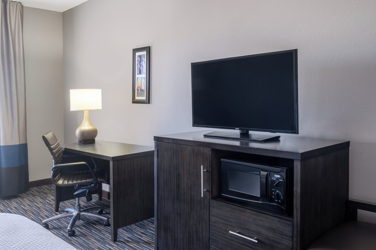 Ein Hotelzimmer mit Schreibtisch, Stuhl, Fernseher, Lampe und einer Mikrowelle.