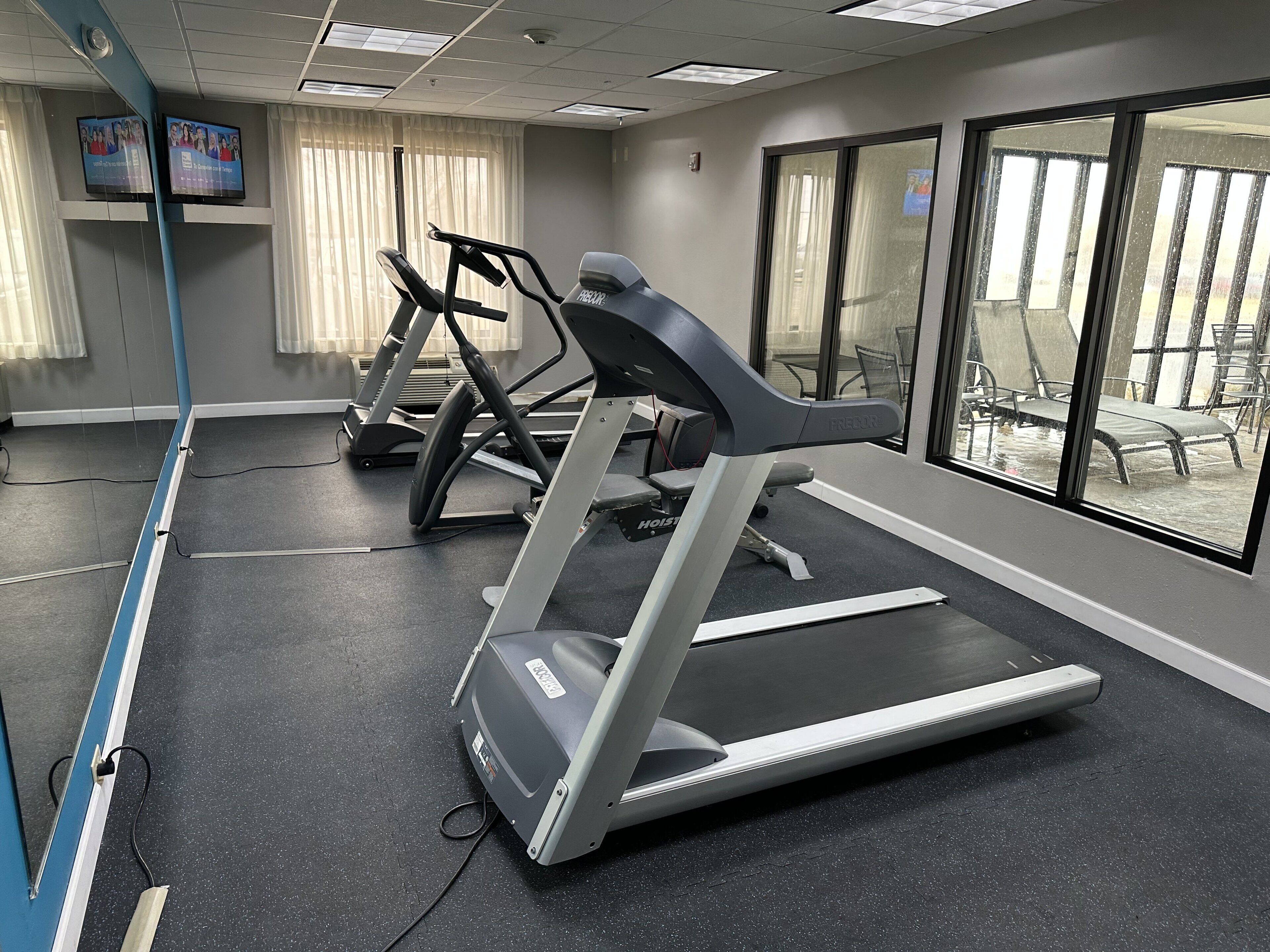Een sportschool met loopbanden en fitnessapparatuur, grote ramen en uitzicht op buiten.