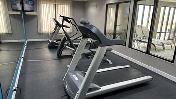 A gym with treadmills and exercise equipment, large windows, and a view of the outside.
