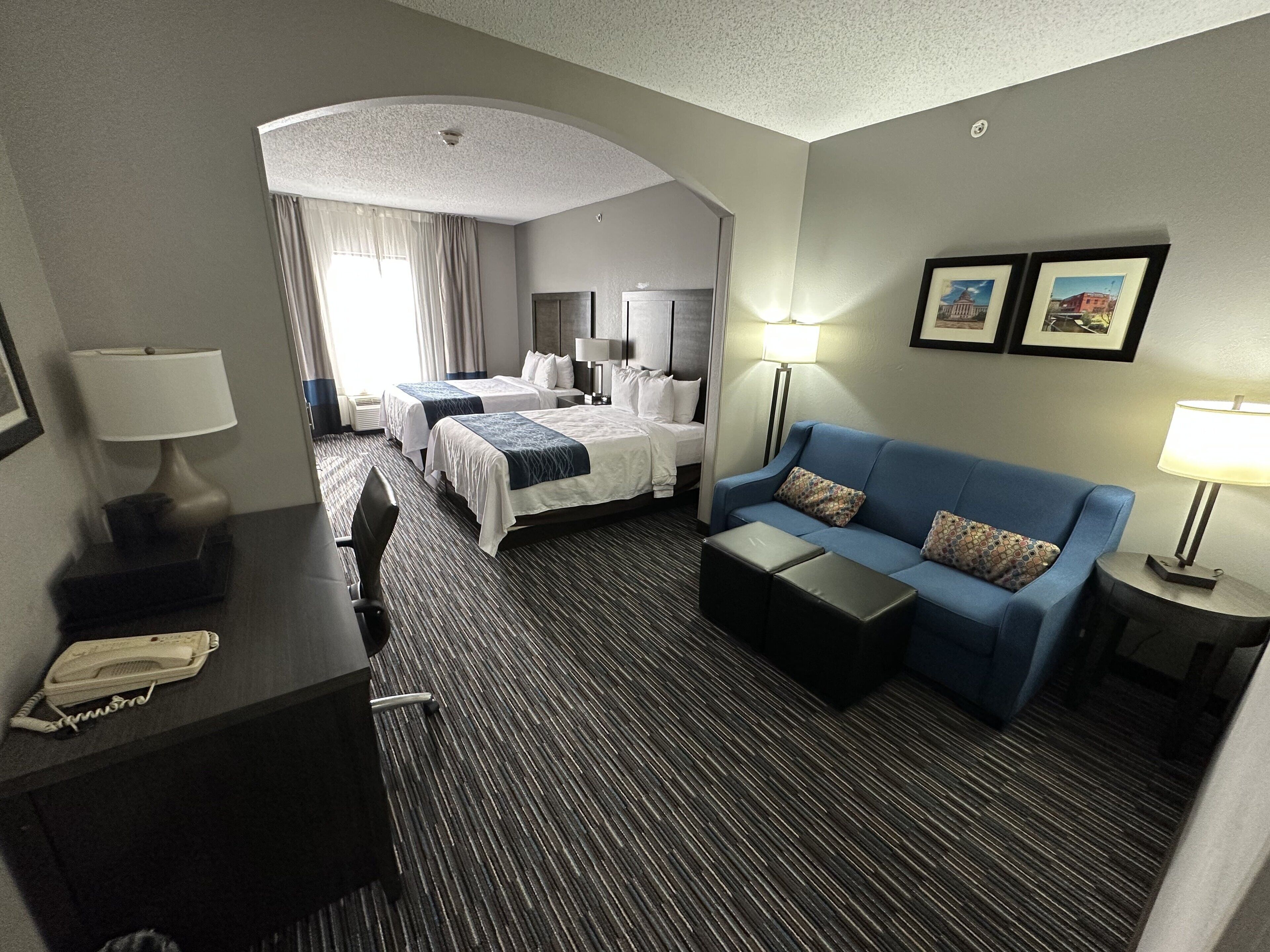 A hotel room with two beds, a blue sofa, a desk with a telephone, and framed pictures on the wall.