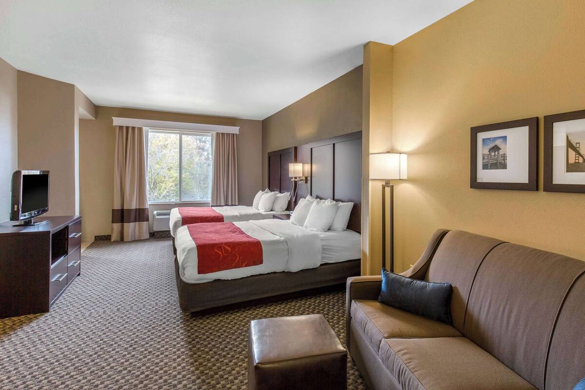 A hotel room with two beds, a sofa, a TV, and a lamp.