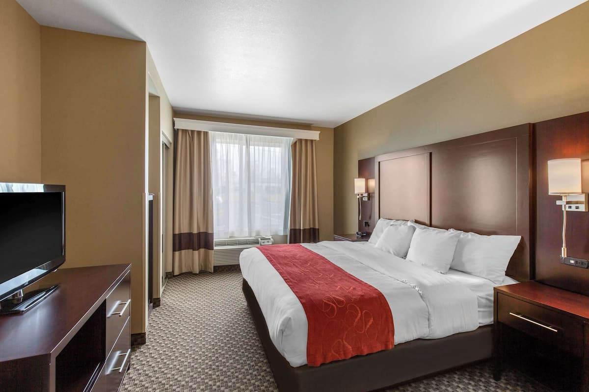 A hotel room with a large bed, a TV, a desk, and a window with curtains.