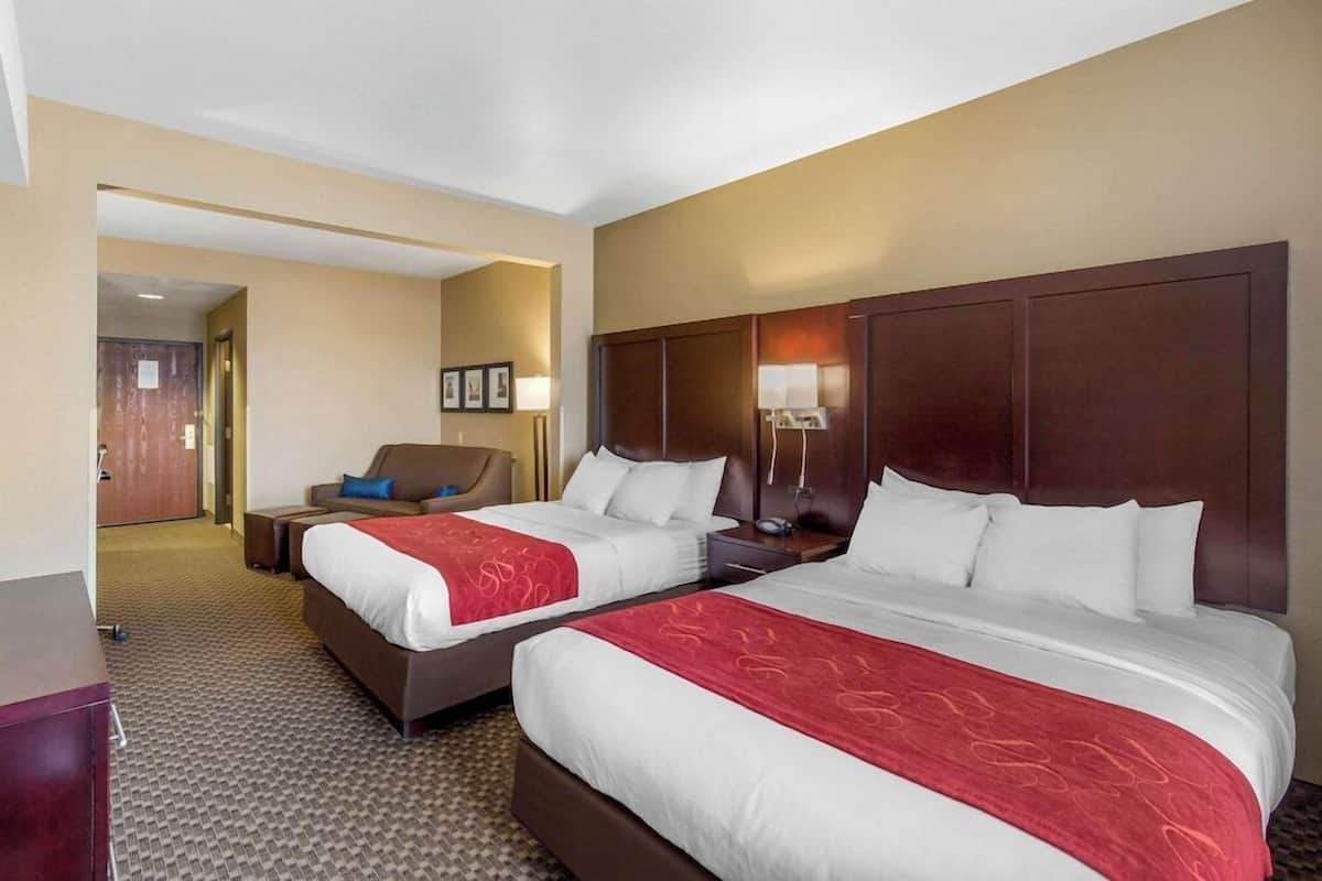 A hotel room with two beds, a desk, a chair, and a door leading to another room.