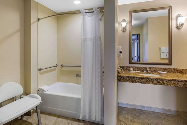 A bathroom with a bathtub, a shower with a white curtain, a vanity with a sink, and a mirror. - Comfort Suites Seaford (Seaford)