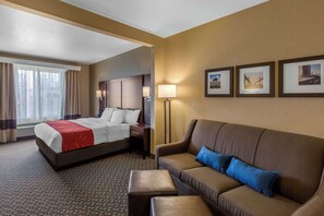A hotel room with a bed, a sofa, a coffee table, and a lamp. There are three framed pictures on the wall. - Comfort Suites Seaford (Seaford)