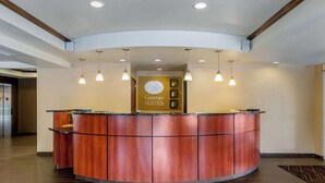 A reception desk with a wooden finish, overhead pendant lighting, and a sign reading "Comfort Suites". - Comfort Suites Seaford (Seaford)