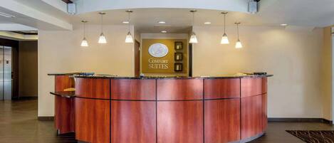 Un comptoir d’accueil avec un revêtement en bois, des luminaires suspendus et une enseigne indiquant « Comfort Suites ».