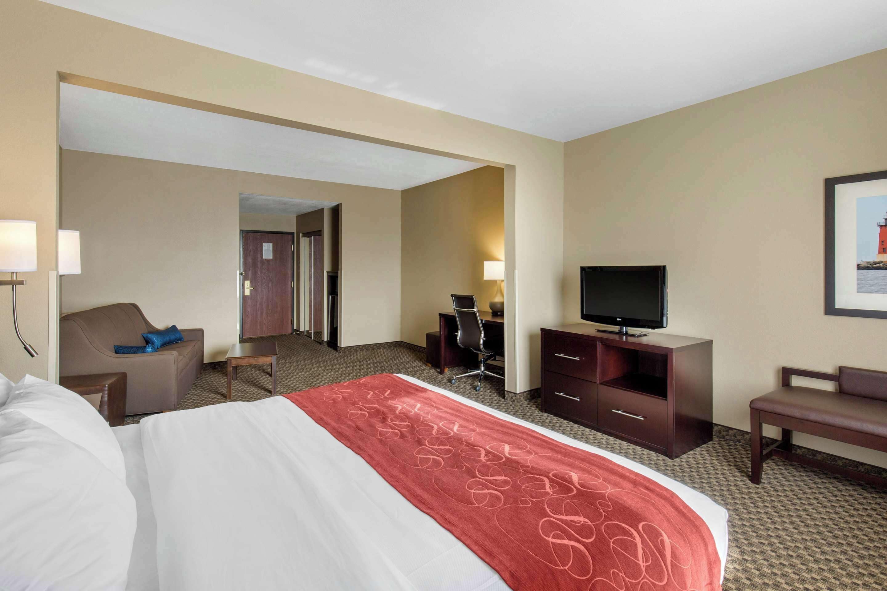 A hotel room with a large bed, a desk, a television, and a seating area.