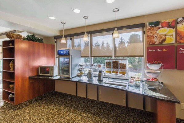 A modern kitchen with a microwave, coffee maker, and fruit bowl. There are hanging lights and a window with a view of trees. - Comfort Suites Seaford (Seaford)