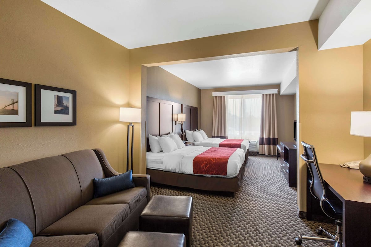 A hotel room with a sofa, two beds, a desk, and a chair.