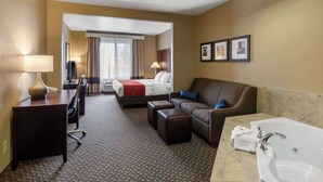 A hotel room with a bed, a sofa, a desk, a chair, a bathroom with a bathtub, and a large window. - Comfort Suites Seaford (Seaford)
