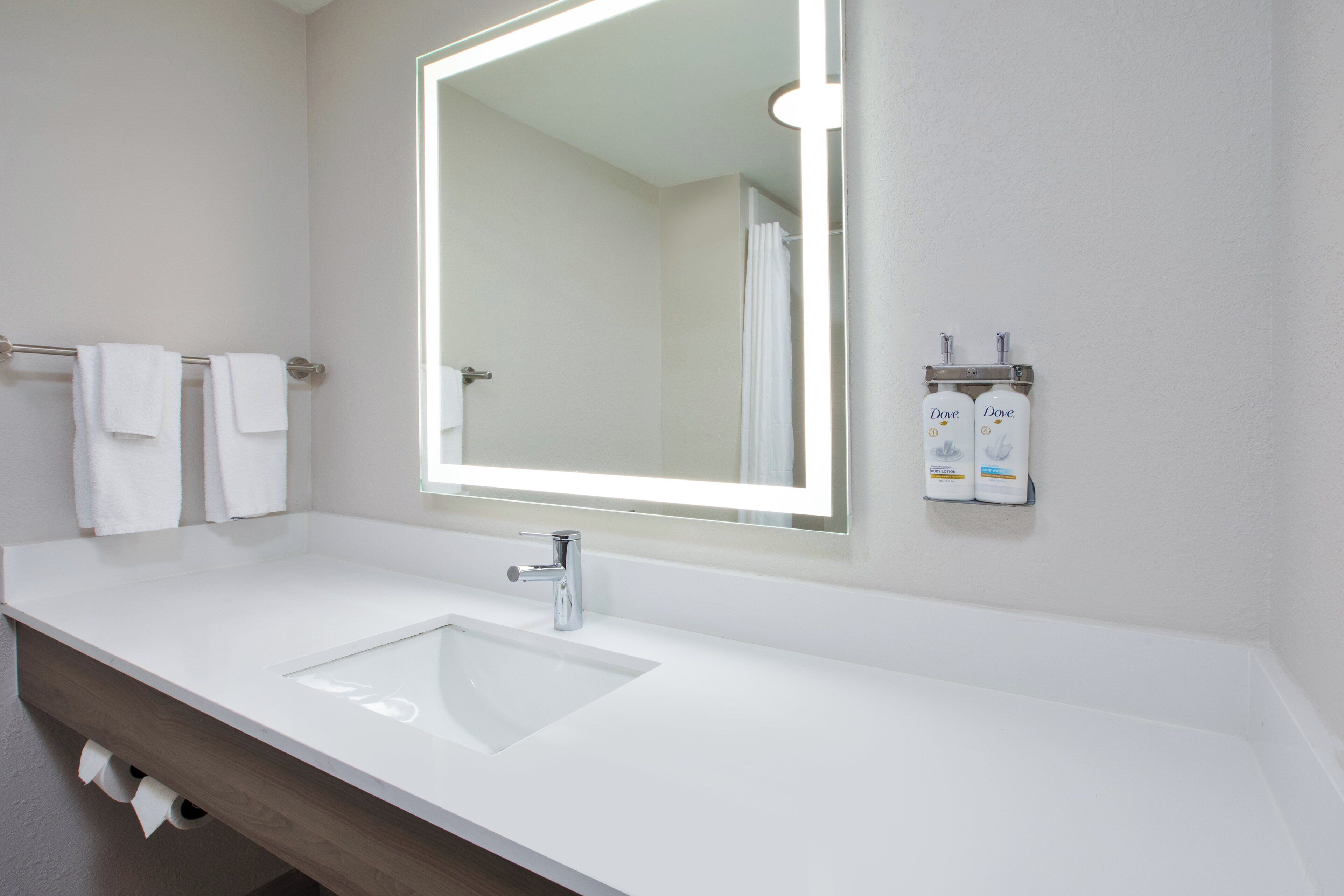 A modern bathroom with a large mirror, a white sink, and two bottles of Dove soap on the wall.
