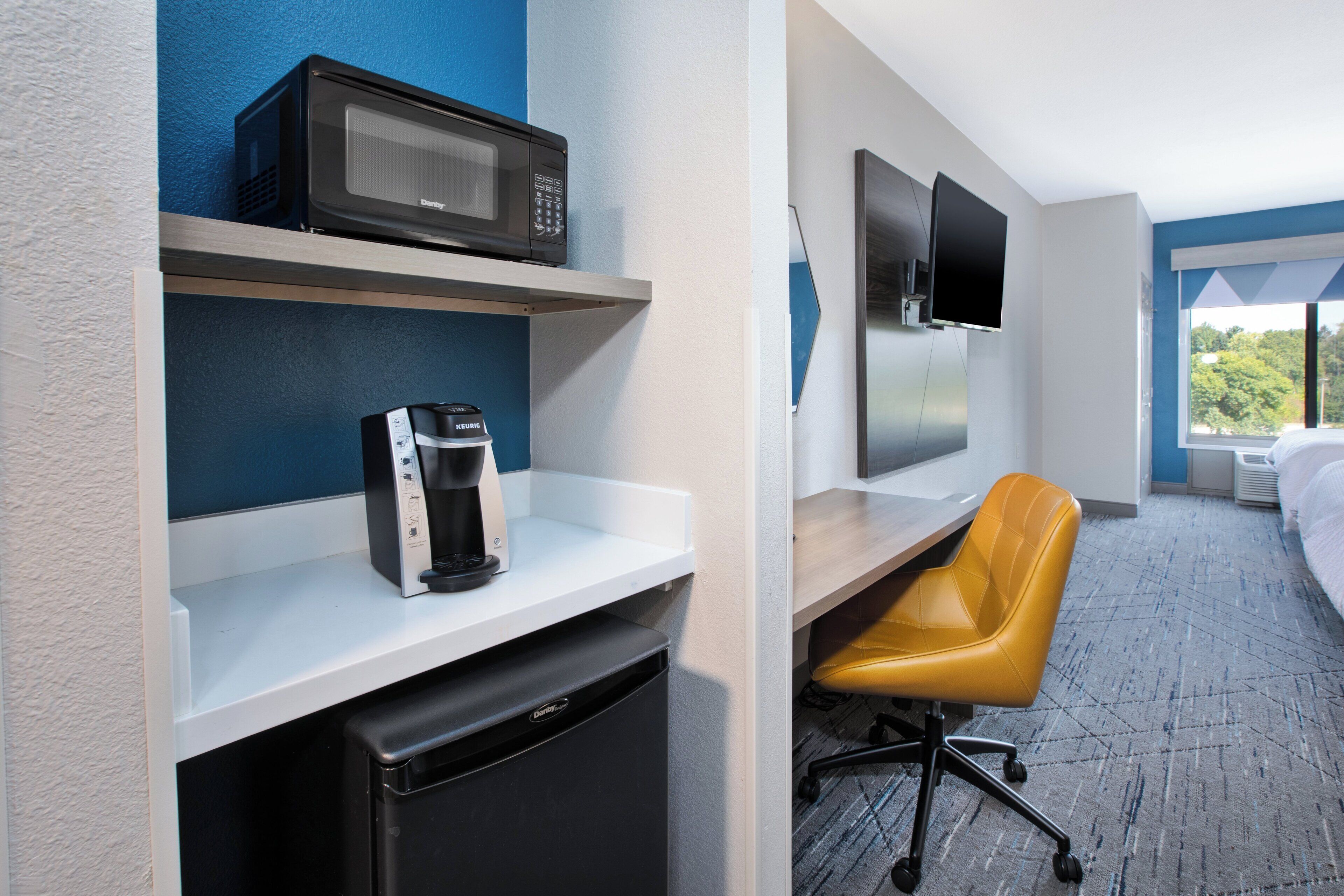Ein Hotelzimmer mit Mikrowelle, Kaffeemaschine und Fernseher an der Wand.