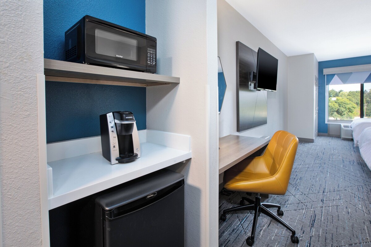 Een hotelkamer met een magnetron, koffiezetapparaat en een televisie aan de muur.